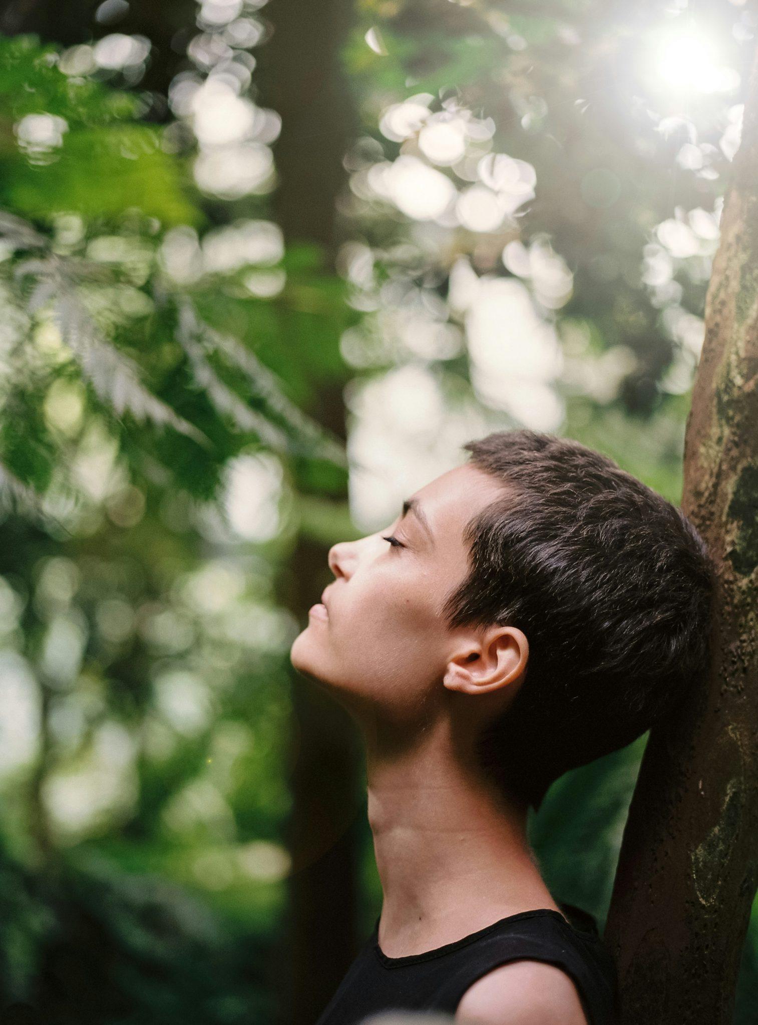 Mujer mirando hacia arriba entre vegetación, con luz suave
